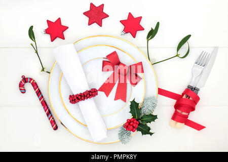 Weihnachtsessen Tisch mit Porzellan Teller, Christbaumkugel Dekorationen, Serviette, winter Holly, Misteln und Tannen auf dem Roten Platz Matte auf weißem Holz Tisch Stockfoto