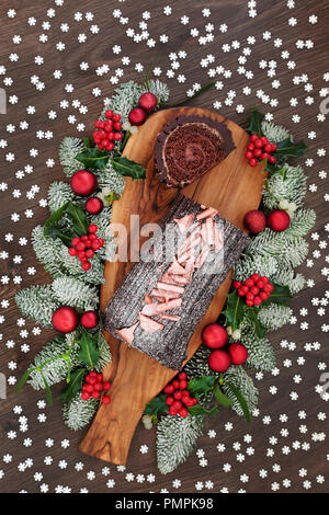 Schokolade yule Kuchen mit Winter Flora von verschneiten Tannen anmelden, Holly und Mistel auf rustikalen Holzbrett und Eiche Tisch Hintergrund. Stockfoto