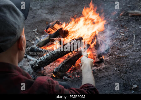 Die Lagerfeuer an einem Wald. Männliche Person in legere Kleidung stellt Stücke Holz in Brand. Stockfoto