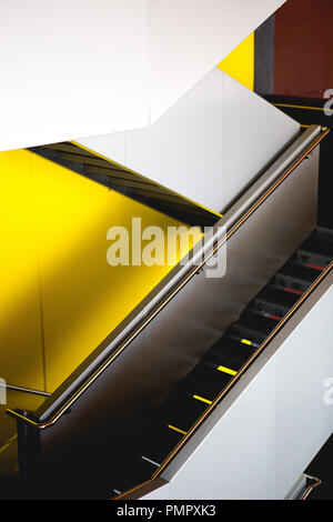 Moderne Treppen/Rolltreppe nach unten im Zickzack gegen eine gelbe Wand im Atrium der in einem modernen Gebäude in der Stadt. Zeitgenössische Architektur & Design Stockfoto