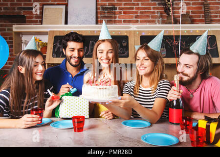 Erregte Frau bereit zum Ausblasen der Kerzen auf weißem Zuckerguss Kuchen am Tisch auf Geburtstagsparty mit Freunden glücklich Stockfoto