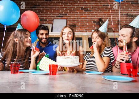 Wunderschöne junge brünette Frau ihren Geburtstag fertig, die Kerzen auf dem Kuchen von einem lächelnden Freunde beobachtete Ausblasen feiern Stockfoto