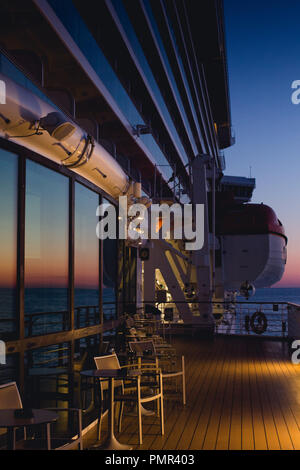 Abend geschossen von den äußeren (Promenade Deck) von einem Kreuzfahrtschiff mit dem Meer im Hintergrund und eine glühende Sonnenuntergang in den Fenstern reflektiert Stockfoto