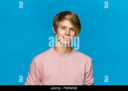 Close up Portrait von lächelnden Blonden Teenager in rosa Bluse vor blauem Hintergrund Stockfoto
