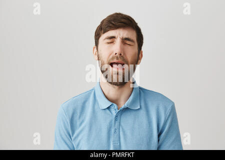 Taille-up Shot aufgeregt stattlichen kaukasischen Kerl in Shirt, Heulen oder weinen, als ob er Baby, stehend über grauen Hintergrund. Frau Passwort auf Laptop, also kann er nicht spielen, bis er Wäsche fertig stellen Stockfoto