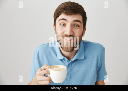 Sie haben etwas auf dem Schnurrbart. Portrait von Lustig verspielt bärtigen Kerl trinken Tasse Cappuccino und in Milch auf Gesicht, ein Lächeln auf den Lippen und sorglos beim Sitzen im Cafe mit Freundin Stockfoto