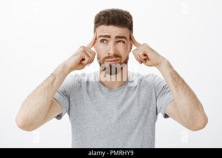 Kerl, der versucht, konzentrieren, denken Neuer Plan. Bestimmt, nachdenklich Schöne charismatische Mann mit Bart und blaue Augen schielen, grinste Sie die Haltefinger auf Tempel mit Schwerpunkt auf importrant Spiel, Konzentration Stockfoto