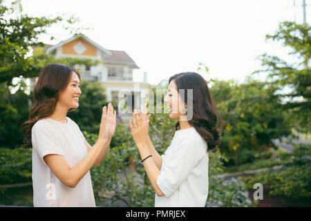 Zwei schöne junge Frauen, die hohe fünf hübschen Mädchen stehen auf im Freien und Spaß haben - Beste Freundinnen, ein Versprechen Stockfoto