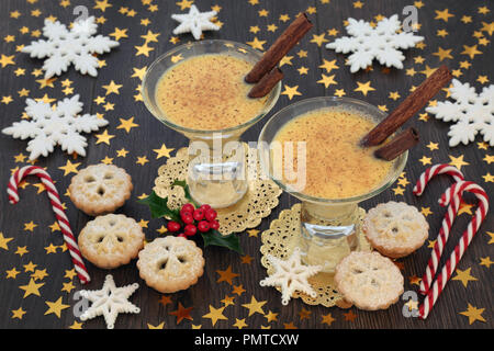 Weihnachtsfeier mit Eierlikör, Torten, Zuckerstangen, Stern und Schneeflocke Dekorationen mit Winter holly mince auf Eiche rustikal Tisch Hintergrund. Stockfoto