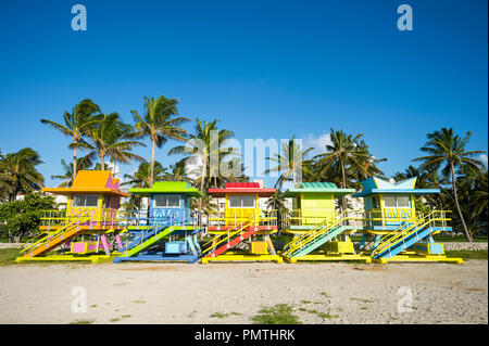 Reihe von bunt bemalten bunte Rettungstürme mit Kokospalmen am Miami Beach Promenade. Stockfoto