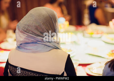 Wunderschöne verschleierte Mädchen in einem förmlichen Outfit Holding ein Mikrofon an etwas mit einer Hand sprechen und einen Vortrag auf einem Menschen Hintergrund zeigt. Stockfoto
