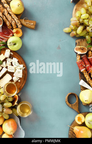 Rahmen der verschiedenen Wein Snacks: Trauben, Pfirsich, Aprikose, Birne, Apfel, jamon, Hartkäse, Brie Käse und Roquefort Käse auf blauen Stein Hintergrund mit Stockfoto