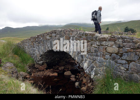 Man Walking auf Melgrave Brücke auf der Corrieyairack Pass Teil der Allgemeinen watet militärischen Straße auf dem Weg zur schottischen Berge Corbett Gairbainn. Stockfoto