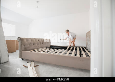 Reife Frau baut ihr Bett in Ihrem neuen Zuhause. Sie ist die Platzierung Holzlatten auf dem Bett. Stockfoto