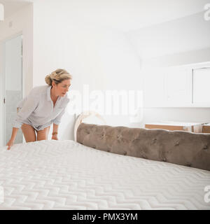 Reife Frau bewegt sich in Ihrem neuen Zuhause. Sie ist die Platzierung Ihrer Matratze auf dem Bett. Stockfoto