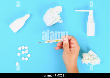 Ein Mann hält ein Thermometer in seine Hand mit einer hohen Temperatur vor einem blauen Tisch mit Tabletten. Top Anzeigen, Kopieren, flach Stockfoto