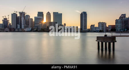 London, England, Großbritannien - 2 September, 2018: Die Sonne hinter einem Cluster von Wolkenkratzern in den Londoner Docklands Canary Wharf Nachbarschaft, mit dem Fluss Stockfoto