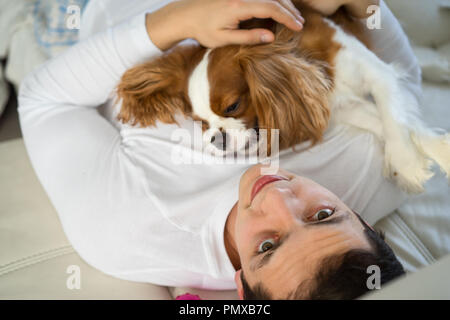 Mensch, der hatte eine gute Zeit mit Hund auf Sofa in den Morgen. Der Cavalier King Charles Spaniel spielen zu Hause Stockfoto