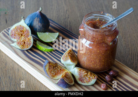 Glas Glas Feigen Marmelade und ein Löffel in, Muttern, Scheiben geschnitten Kalk und Feigen auf einem Holztisch Hintergrund Stockfoto