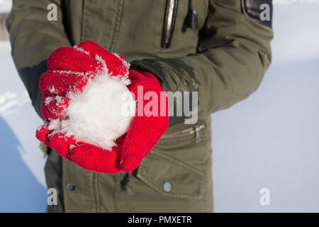 Nahaufnahme der Hände in roten Handschuhe holding Schneeball im Winter im Freien Stockfoto