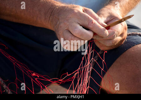 Fischer Hände Instandsetzung sein rot Fischernetz mit Nadel, Nahaufnahme, Detail Stockfoto