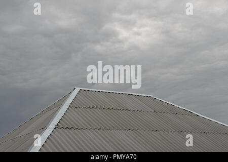 Close-up grau Asbestzement wave Blatt Walmdach mit verzinkter Stahl ridge und hip Blinken auf Grau bewölkter Himmel Hintergrund. Stockfoto