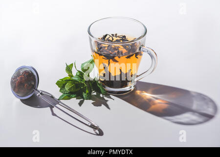 Tasse schwarzen Tee, Minze und Teesieb auf weißen Tischplatte Stockfoto