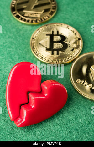Gold physischen Bitcoin, Litecoin und des Astraleums Münzen mit gebrochenen Herzen auf grünem Hintergrund. Crypto Währung Markt Pause oder keine Liebe abstraktes Konzept. Stockfoto
