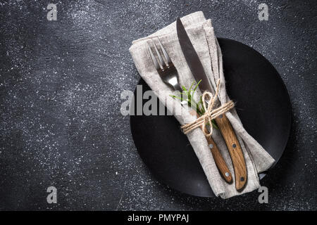 Schwarz Teller, Besteck und Serviette auf steinernen Tisch Ansicht von oben. Stockfoto