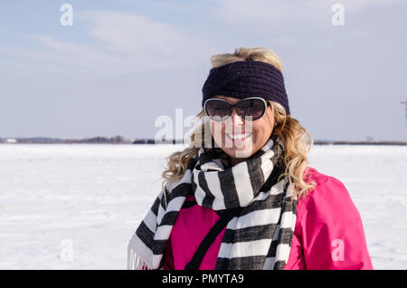 Attraktive erwachsenen Frau posiert im Bauernhof Feld im Schnee An einem kalten Wintertag abgedeckt, das Tragen eines ski Jacke und Hut Stockfoto