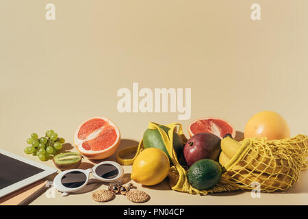 Sonnenbrillen, Ohrringe, digital Tablet und reifen Früchten in string Beutel auf Braun Stockfoto