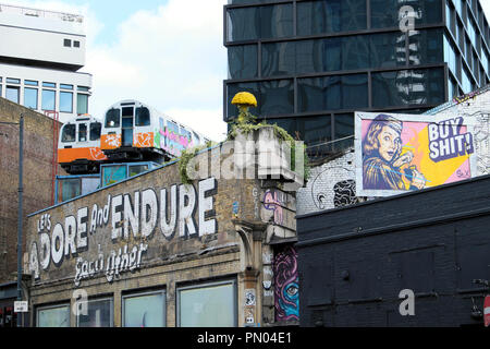 'Laßt uns anbeten und Ertragen, Einander "Graffiti an der Wand mit Waggons auf dem Dach Great Eastern Street Art in Shoreditch East London UK KATHY DEWITT Stockfoto