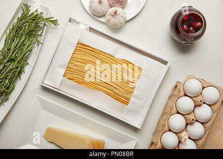 Blick von oben auf die Anordnung der Ungekochtes macaroni, Knoblauch, Rosmarin und Käse zum Kochen Pasta auf weißen Tischplatte Stockfoto