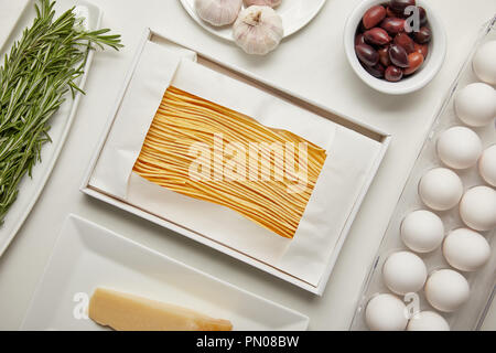 Blick von oben auf die Anordnung der Ungekochtes macaroni, Knoblauch, Rosmarin und Käse zum Kochen Pasta auf weißen Tischplatte Stockfoto