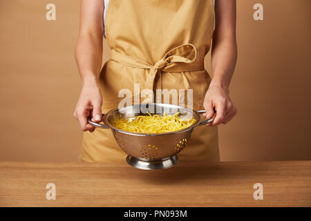 7/8 Schoß der Frau in gelber Schürze holding Sieb mit Spaghetti Stockfoto