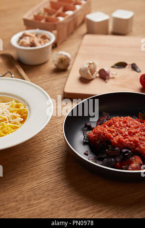 Nahaufnahme der Teller mit Spaghetti und Tomatensoße in der Pfanne auf hölzernen Tisch Stockfoto