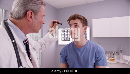 Mitte - gealterte Arzt prüft die Augen der jungen erwachsenen männlichen Patienten. Stockfoto