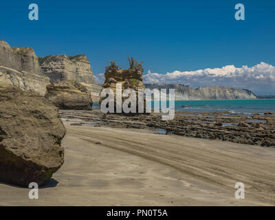 Sea Stacks und steilen Klippen erheben sich über den Sandstrand entlang Kap-entführer an einem schönen sonnigen Tag an der Hawkes Bay in Neuseeland. Stockfoto