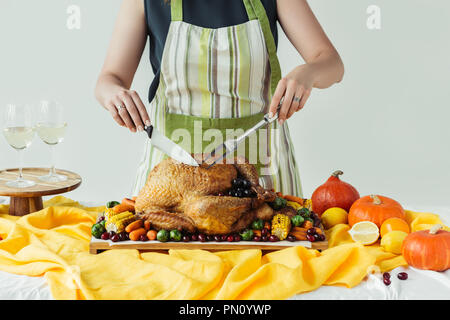 Teilweise mit Blick auf die Frau im Vorfeld schneiden gebratener Truthahn für Thanksgiving Abendessen auf grauem Hintergrund Stockfoto