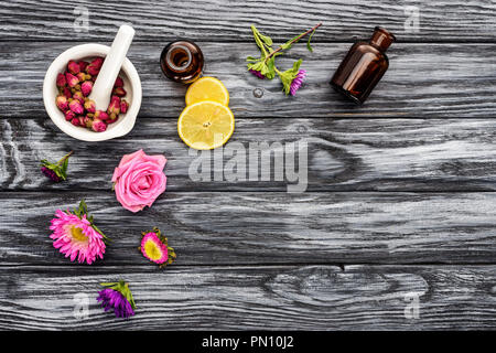 Blick von oben auf die Flaschen natürliche pflanzliche ätherische Öle, Blumen und Pistill mit Mörtel auf hölzernen Tisch Stockfoto