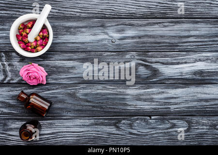 Ansicht von Flaschen mit natürlichen pflanzlichen ätherischen Ölen und Rosen auf graue Oberfläche Stockfoto