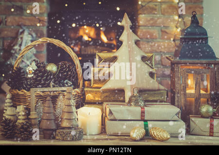 Weihnachten Einstellung, Schmuck, Geschenke und Tannenzapfen, Baum auf dem Tisch vor einem Kamin mit Kaminofen, Star lights und Girlanden, lit. l Stockfoto