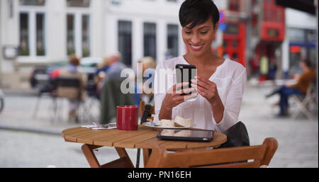 Hübsche schwarze Frau im Cafe in Brügge video Chats mit einem Freund auf dem Smartphone Stockfoto