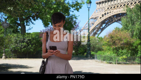 Fröhliche gemischten Rasse Frau liest Texte auf dem Smartphone vor dem Eiffelturm. Stockfoto