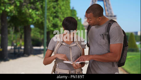 Afrikanischer Mann und Frau mit dem Rucksack quer durch Europa auf der Suche nach Reiseführer in Paris Stockfoto