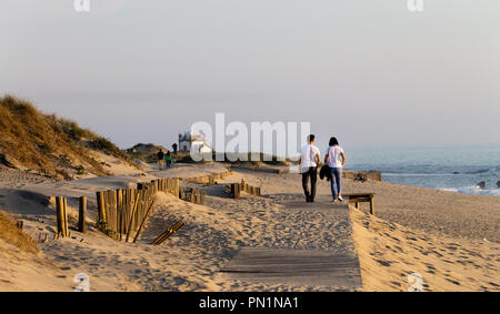 Ein junges Paar Spaziergänge entlang der Promenade in der Nähe der Küste, mit einer Kapelle im Hintergrund. Stockfoto