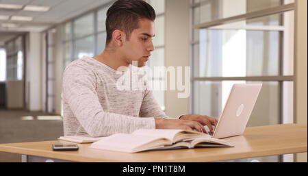 Tausendjährige Hispanic Student in Campus Bibliothek mit Laptop und Mobiltelefon Stockfoto