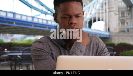 Nahaufnahme der junge schwarze Mann sitzt in der Nähe der Tower Bridge, der an einem Notebook arbeitet Stockfoto