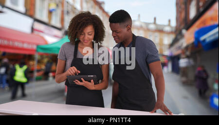 Zwei glückliche Kellner mit digitalen Tablette zu beliebten Straßenmarkt in Brixton Stockfoto