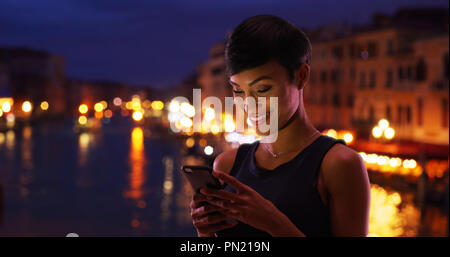 Hübsche schwarze Frau in Venedig Italien reisen liest ihr Handy Nachrichten lächelnd Stockfoto